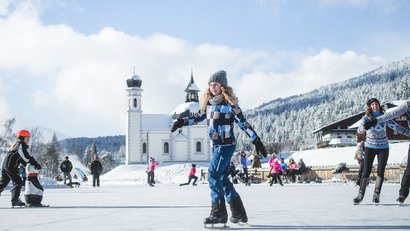 Menschen beim Schlittschuhlaufen auf einer gefrorenen Fläche vor einer Kirche im Winter