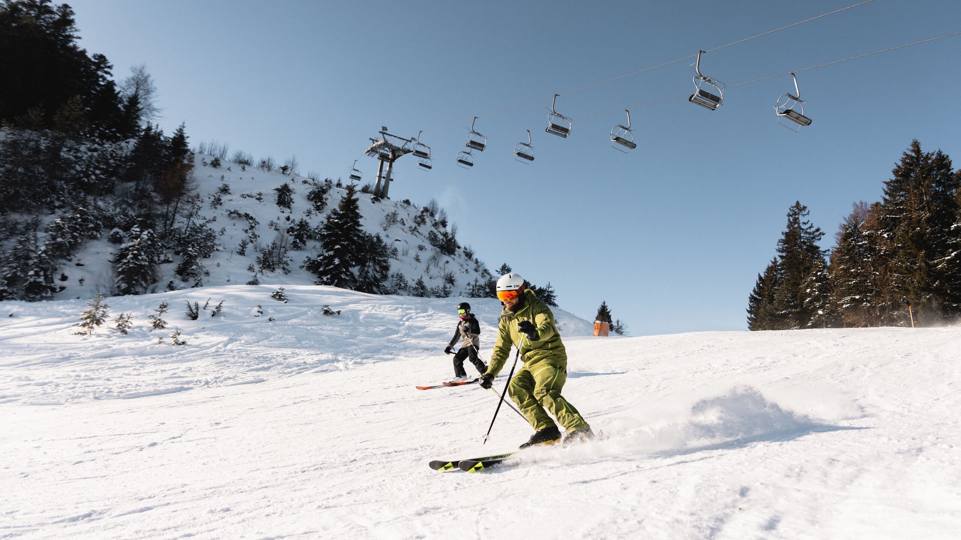 Zwei Skifahrer fahren auf schneebedecktem Hang unter Sessellift