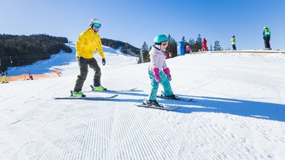 Erwachsener lehrt Kind Ski fahren auf sonnigem verschneiten Hang