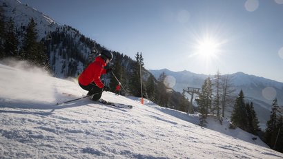 Skifahrer in roter Jacke fährt bei Sonnenschein auf verschneiter Piste
