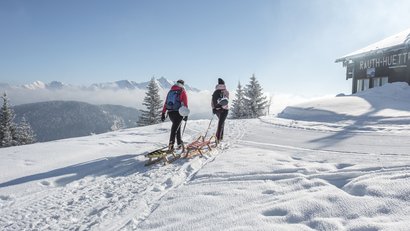 Zwei Wanderer ziehen Schlitten durch verschneite Berglandschaft bei klarem Himmel